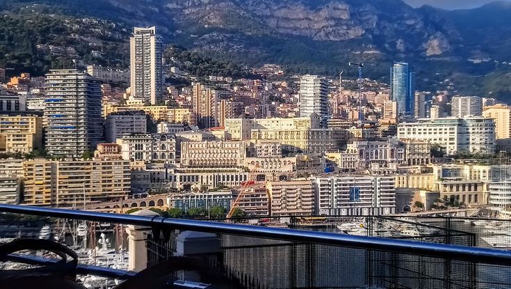 Cityscape of Monaco, with many high-rise buildings nestled against a mountainous backdrop under a sunny sky.