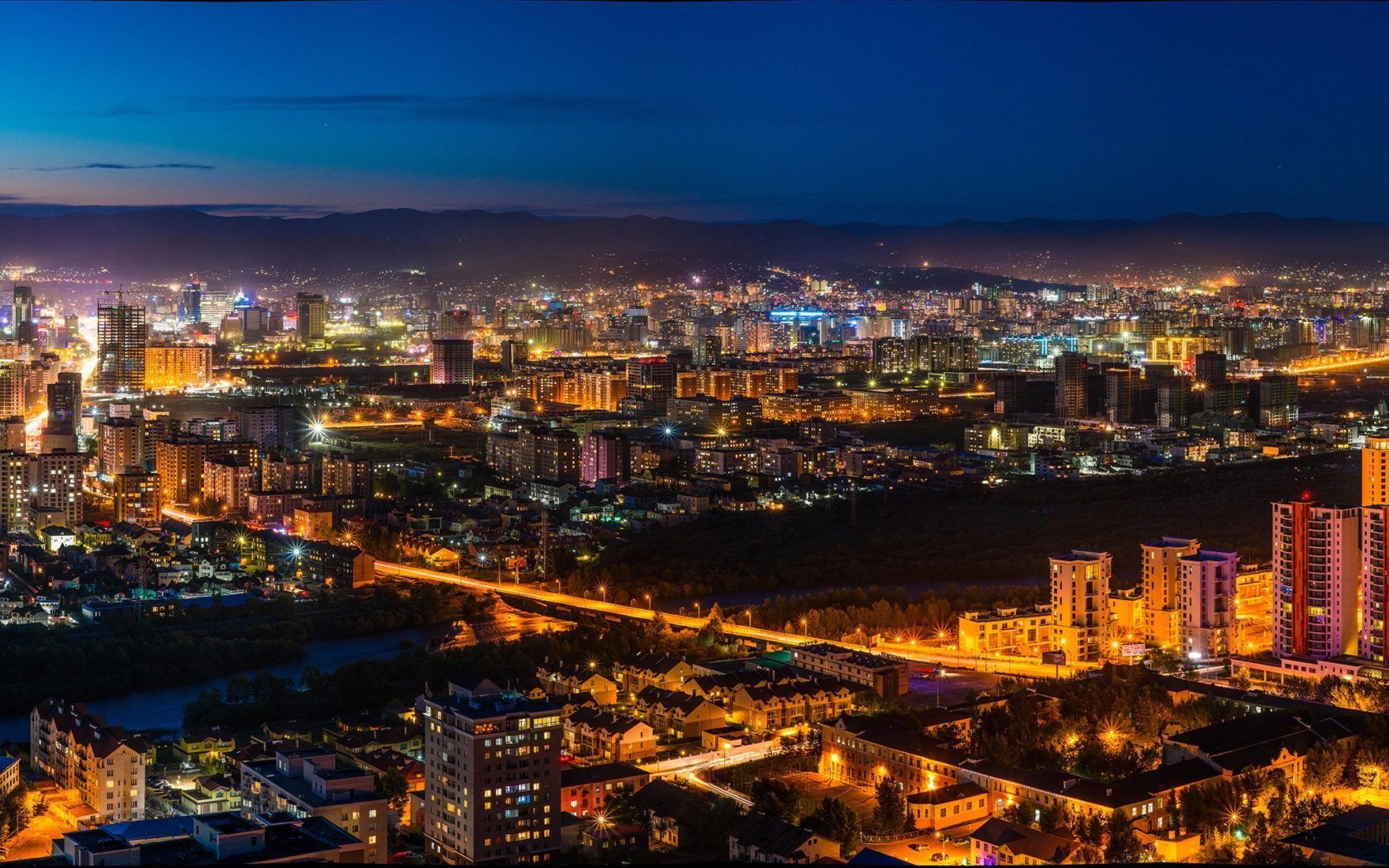 Nighttime cityscape with bright lights against a dark blue sky, illuminating buildings and streets.
