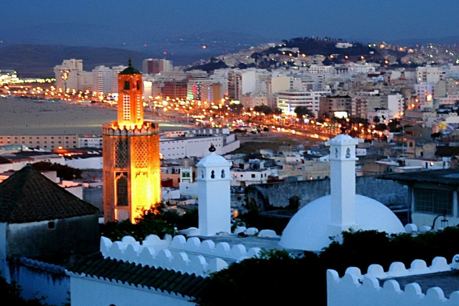Night view of Tangier, Morocco, with illuminated mosque minaret and city lights against a dark sky.