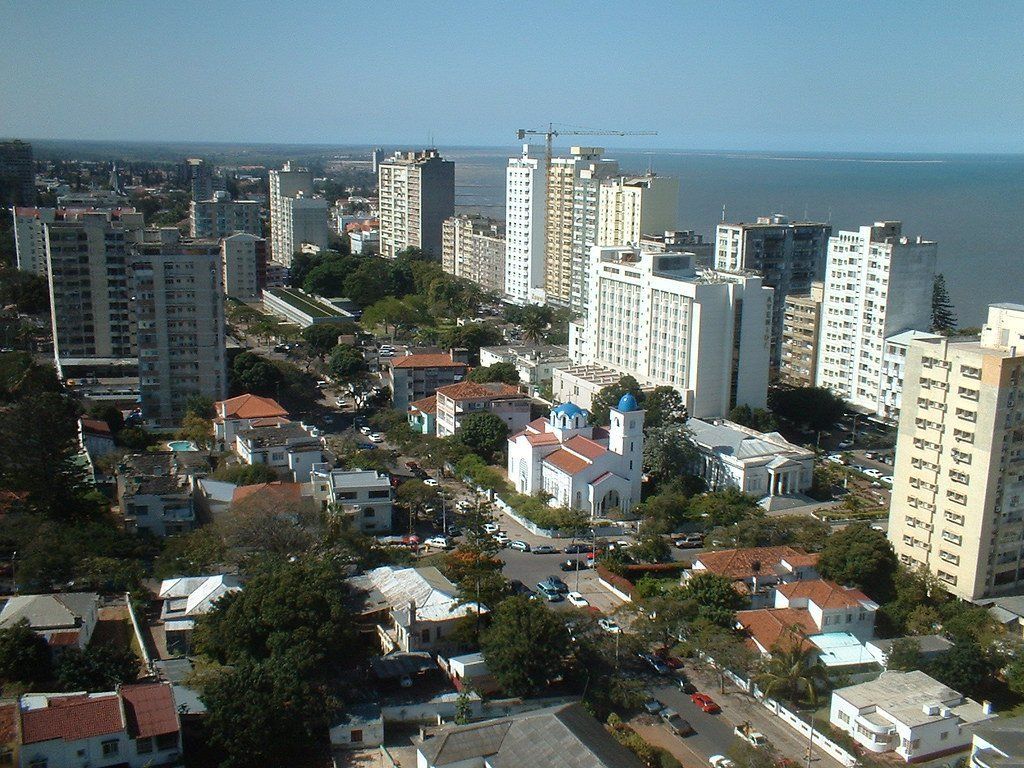 High-angle view of a city with white buildings, a church, and the ocean in the background under a clear blue sky.