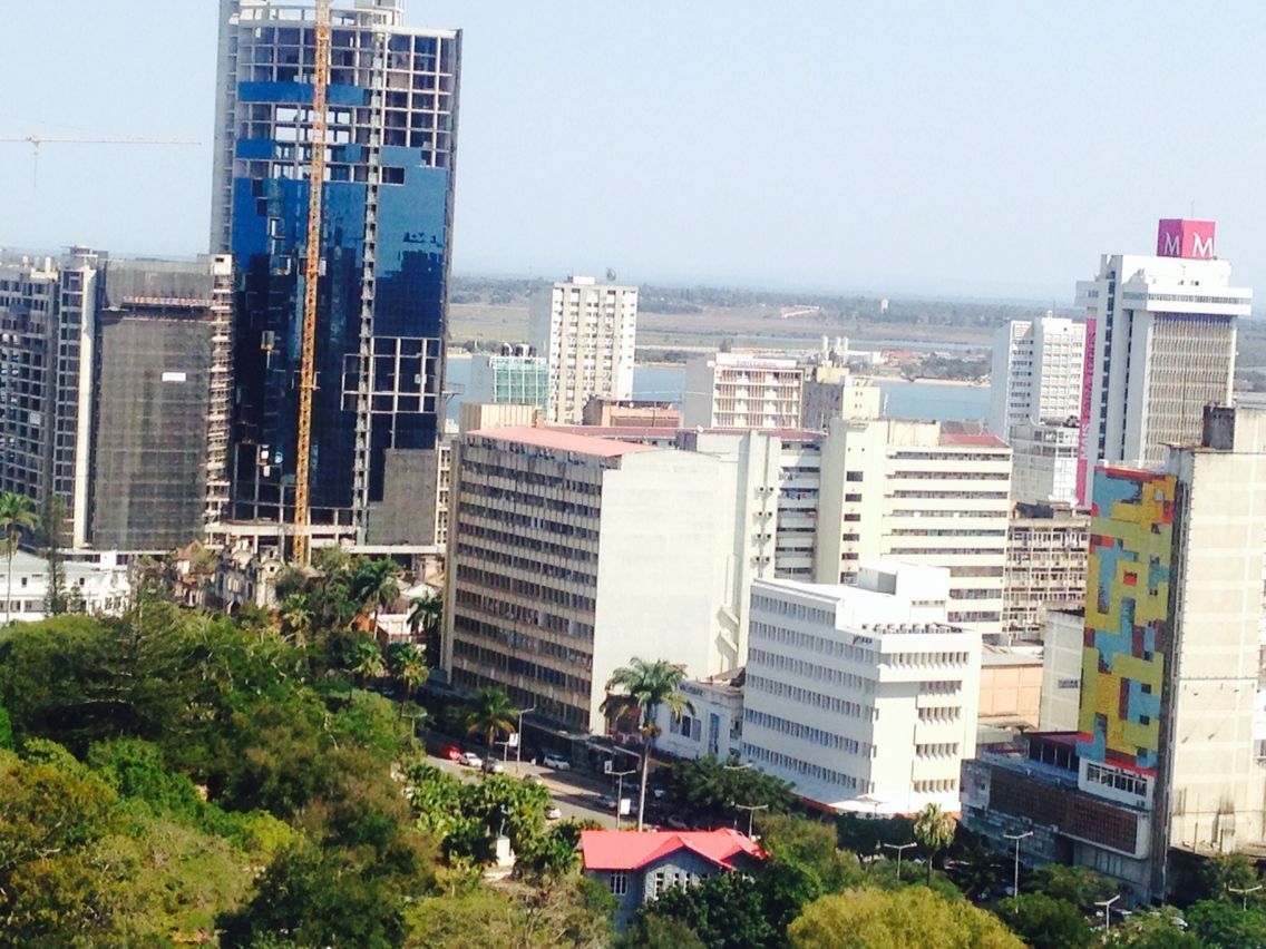 Cityscape with tall buildings, a blue-glass skyscraper under construction, and green trees in the foreground.