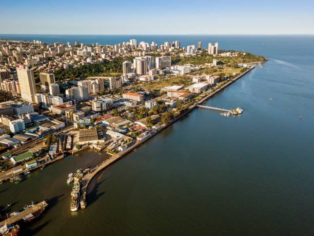 Aerial view of a coastal city with tall buildings along the shoreline. The water is dark blue, and the sky is clear.