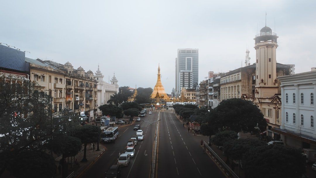 View of a wide city street in Yangon, Myanmar, with a golden pagoda in the distance; buildings line the road under a cloudy sky.