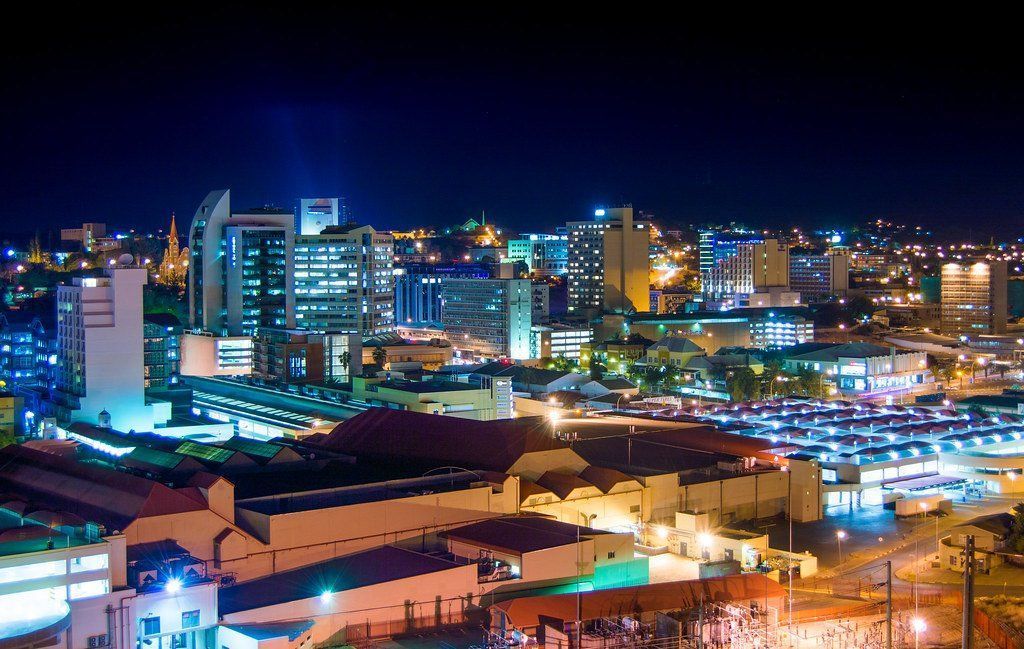 Nighttime cityscape with illuminated buildings under a dark blue sky. Several tall buildings stand out amidst the skyline.