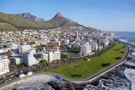 Coastal city of Cape Town, South Africa, with Table Mountain and Lion's Head in the background. Ocean and greenery in the foreground.