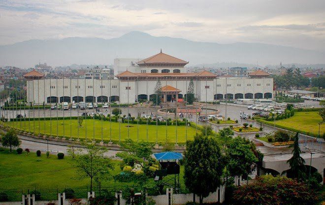 Parliament building in Kathmandu, Nepal; a large white structure with red-tiled roof and manicured lawns in front. Mountain visible in the distance.