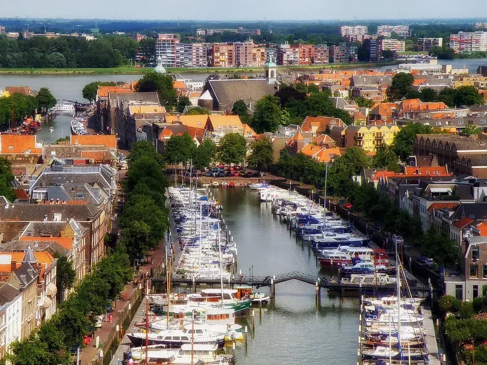 Aerial view of a harbor in a European city. Boats line the canal, with buildings, a church, and apartments in the background.
