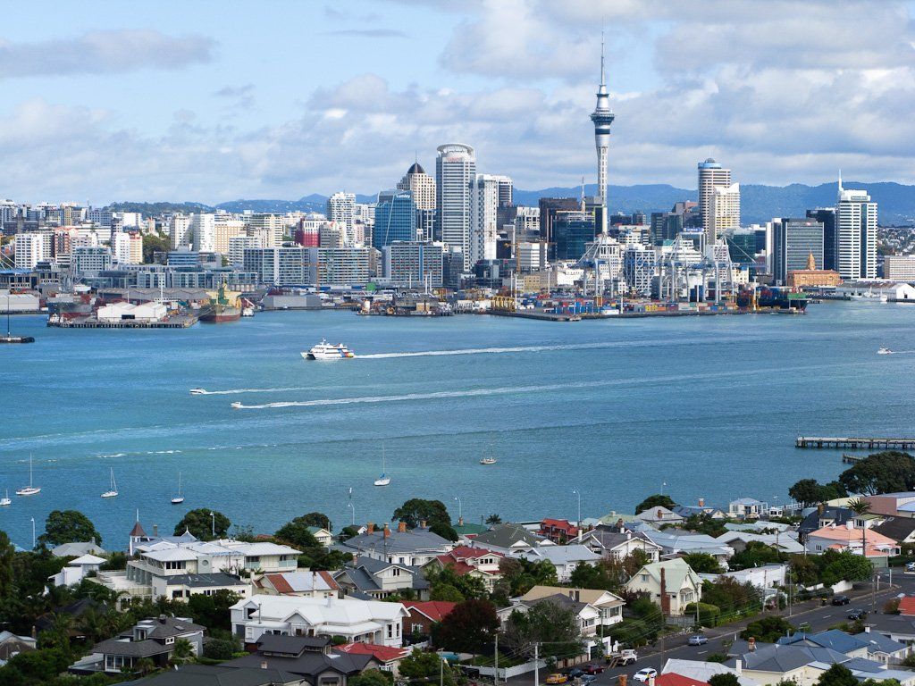 Auckland, New Zealand, cityscape with harbor, boats, and the Sky Tower prominent in the center. Residential neighborhood in the foreground.