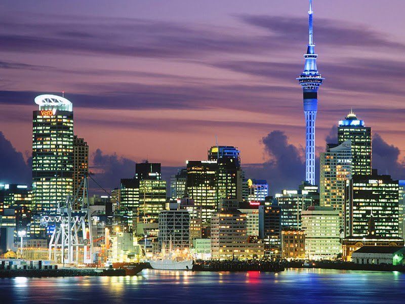 Auckland, New Zealand skyline at dusk with the Sky Tower illuminated against a purple and orange sky.