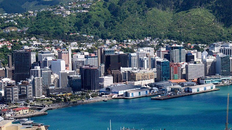 City skyline on a harbor with mountains in the background. Buildings of varying heights line the waterfront.