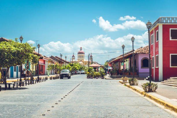 Cobblestone street in Granada, Nicaragua, lined with colorful buildings and leading to a cathedral under a blue sky.