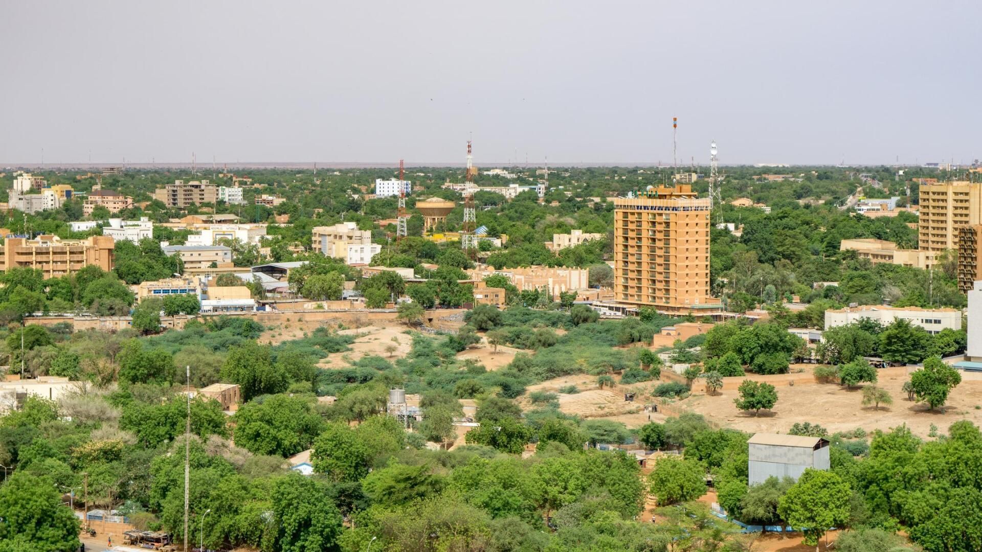 Aerial view of Niamey, Niger, featuring a mix of beige buildings and lush green trees under a hazy sky.