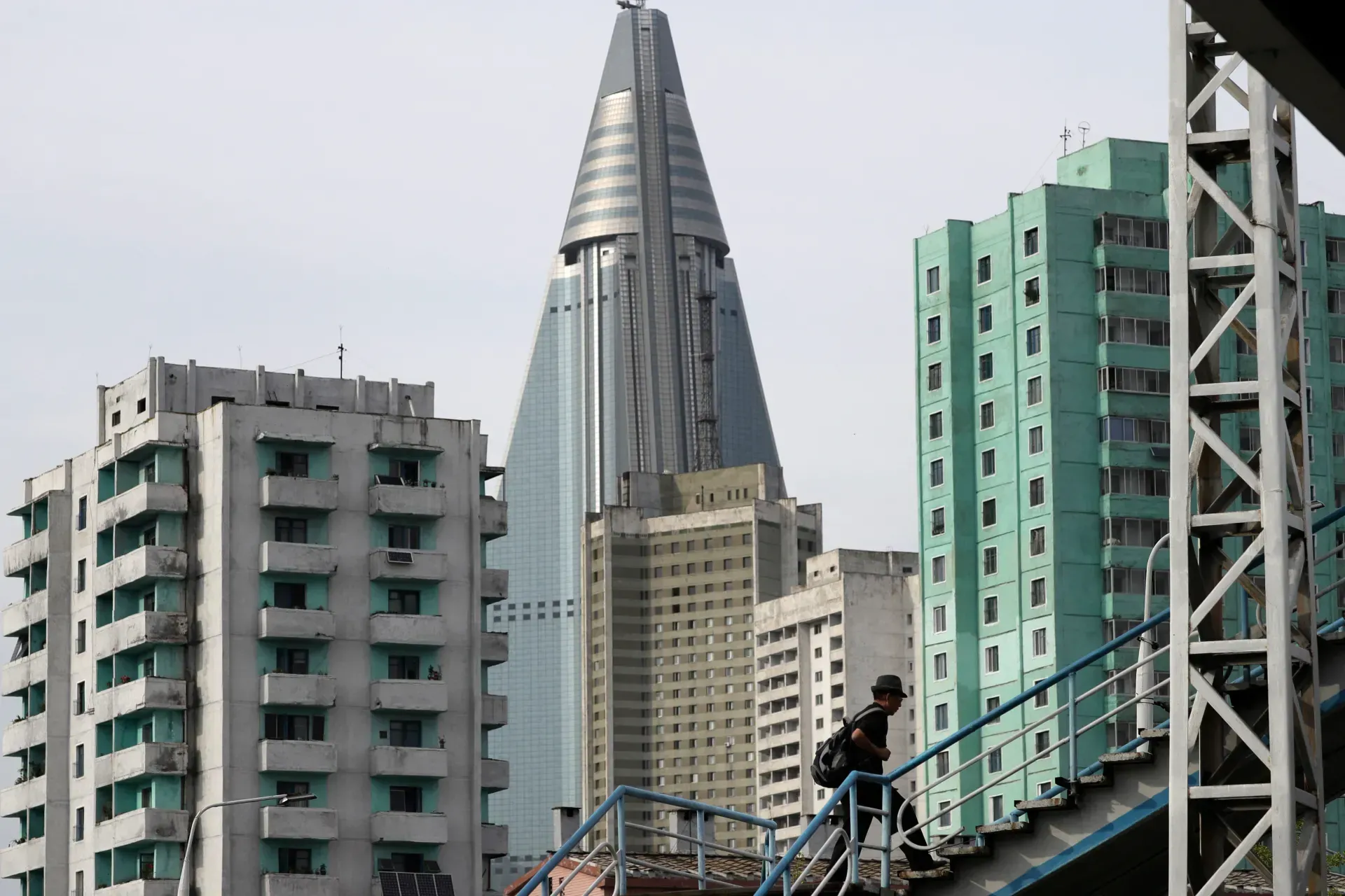 Man walking down stairs in front of apartment buildings in Pyongyang, North Korea. The Ryugyong Hotel dominates the background.