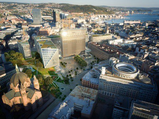 Aerial view of a modern city with a large, sunlit skyscraper and a green park area.