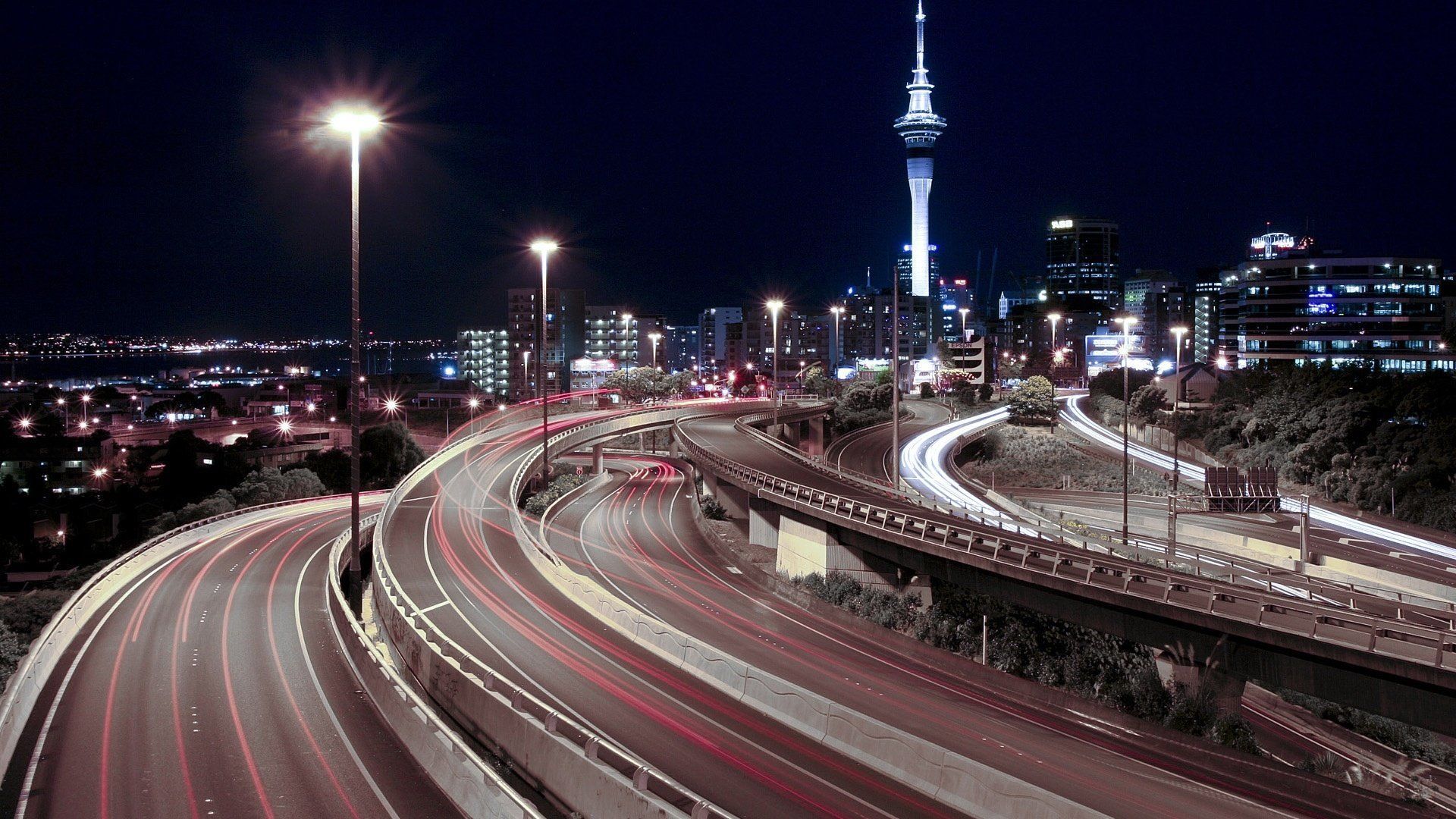 Night view of Auckland, New Zealand, with the Sky Tower prominent. Highway traffic streaks through the foreground.