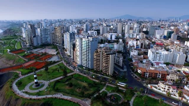 Aerial view of Lima, Peru, with a coastal park and towering buildings under a clear sky.
