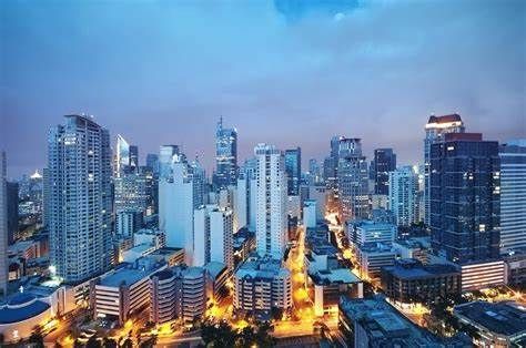City skyline at dusk with numerous illuminated skyscrapers under a blue sky.