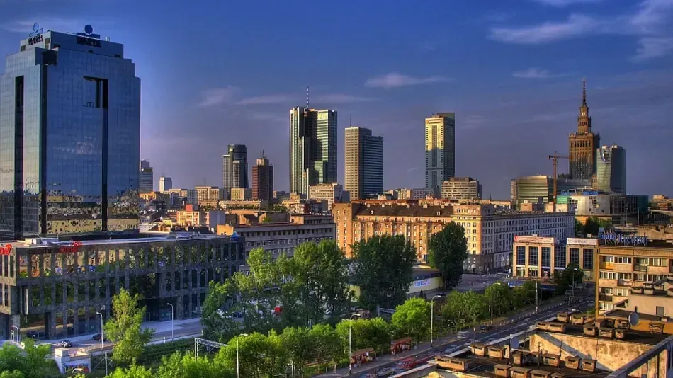 Warsaw, Poland skyline featuring modern skyscrapers against a blue sky, with some older buildings in the foreground.