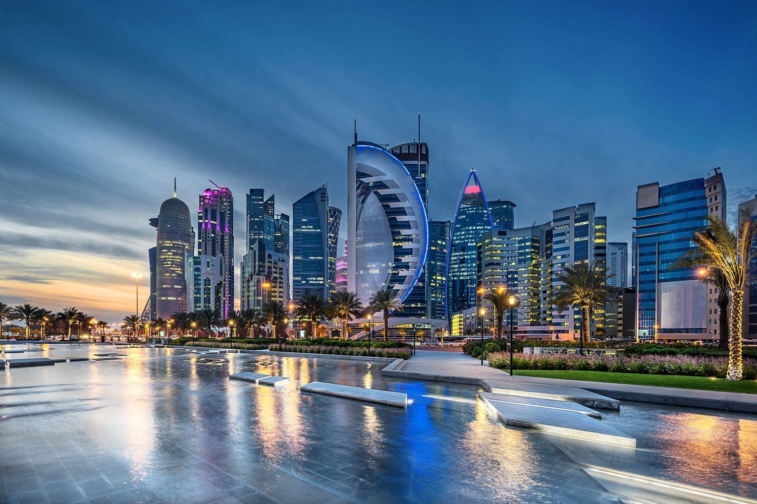 Doha, Qatar skyline at dusk, reflected in water. Modern skyscrapers illuminated with colorful lights.