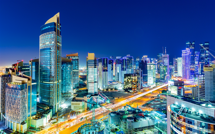 Nighttime cityscape of Doha, Qatar, with brightly lit modern skyscrapers and highways under a deep blue sky.