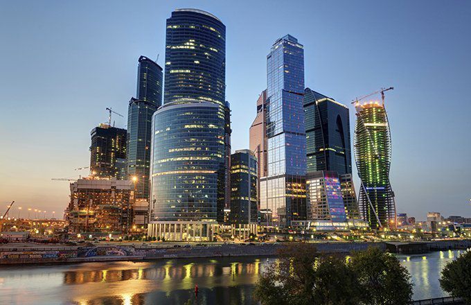 Modern skyscrapers at dusk reflect in a river in Moscow.