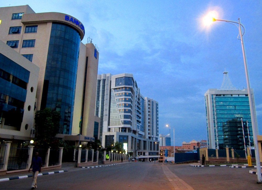 Buildings line a quiet street at dusk, lit by streetlights. A person walks on the sidewalk.
