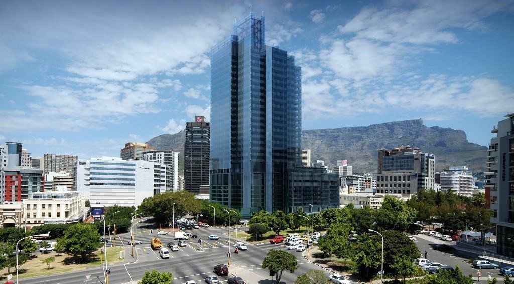 Cityscape with a tall glass skyscraper, roads with cars, and Table Mountain in the background under a blue sky.