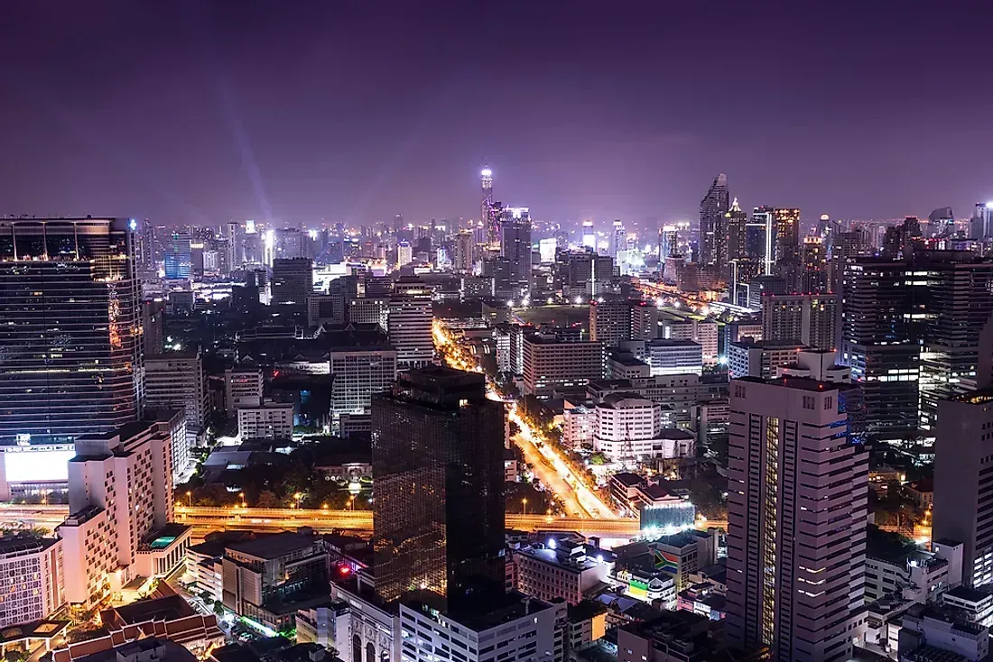 Nighttime cityscape with illuminated skyscrapers, roads, and a purple-hued sky, likely depicting a vibrant urban area.