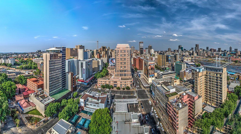 Panoramic aerial view of Johannesburg, South Africa. City skyline with tall buildings under a blue sky.