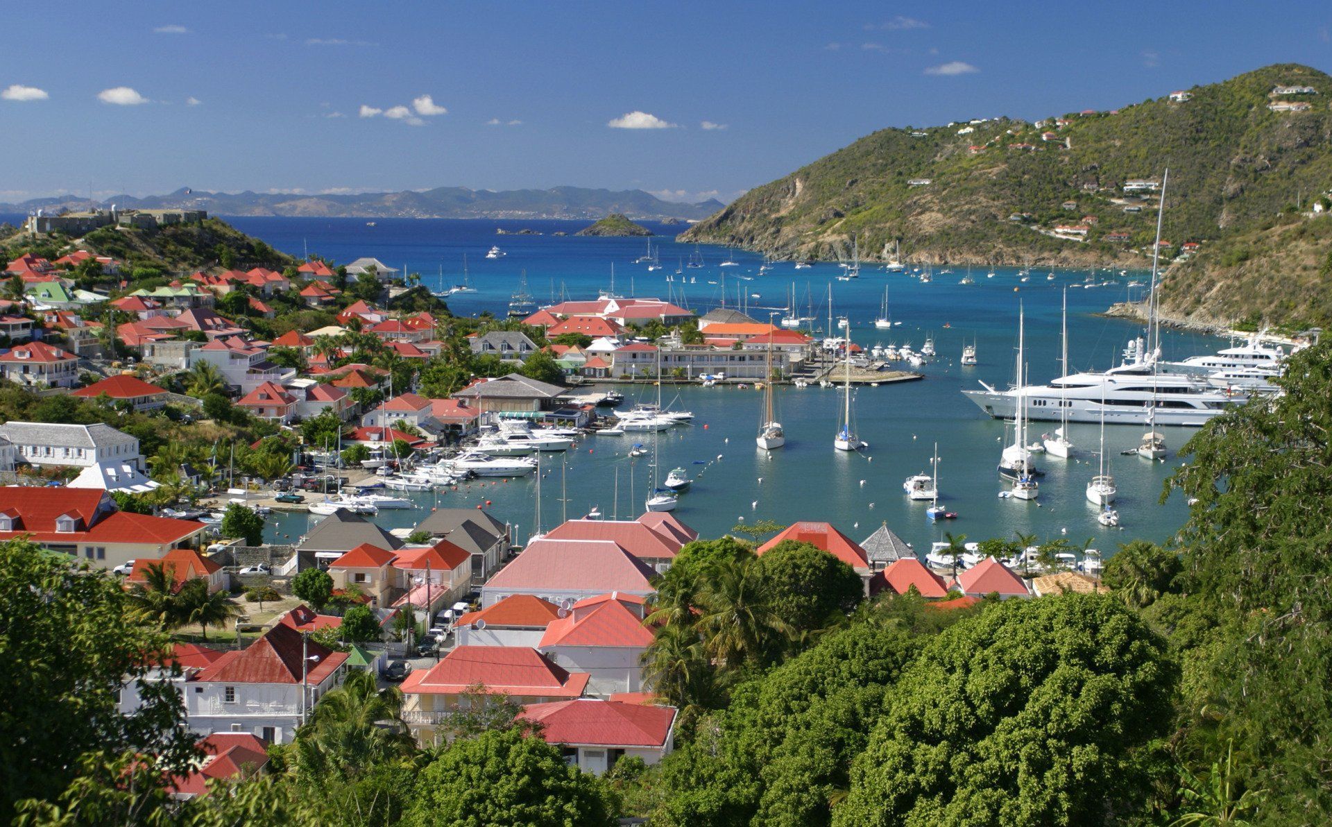 A scenic bay in Gustavia, St. Barthélemy, with a harbor full of boats and hillside homes with red roofs.