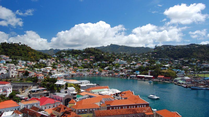 A coastal town with colorful buildings and red tile roofs, nestled beside a blue bay under a cloudy sky.