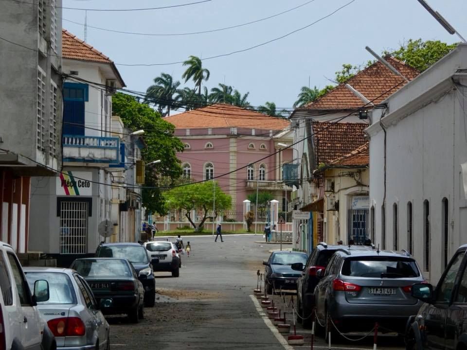 Street view in a town with parked cars, colonial-style buildings, and a pink building with a large facade at the end of the street.