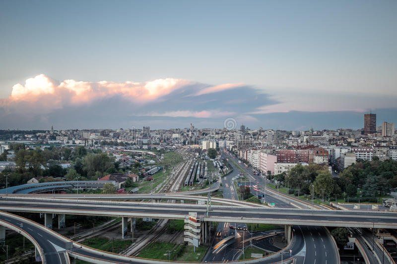 Elevated view of a city with a complex highway interchange in the foreground under a cloudy sky.