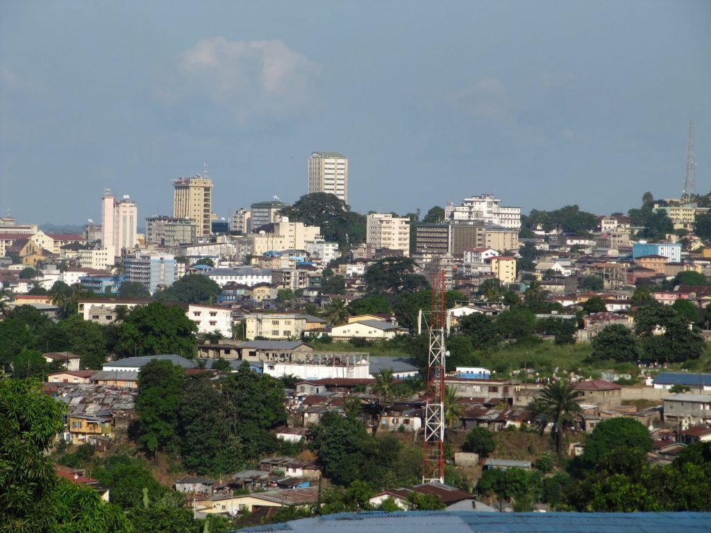 Cityscape of buildings on a hillside, including skyscrapers and residential areas, under a clear sky.