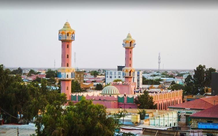 Pink mosque with two minarets and a green dome, in a city setting.