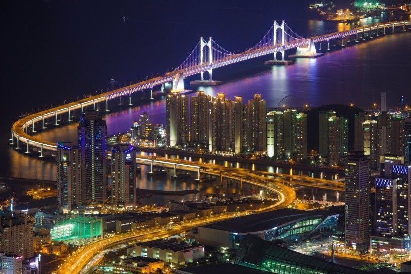 Night view of Busan, South Korea, featuring illuminated Gwangan Bridge and city lights reflecting on the water.