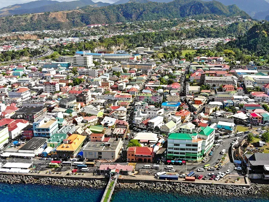 Aerial view of a colorful coastal city nestled between a mountain range and the ocean. Buildings are various colors with a pier extending into the water.