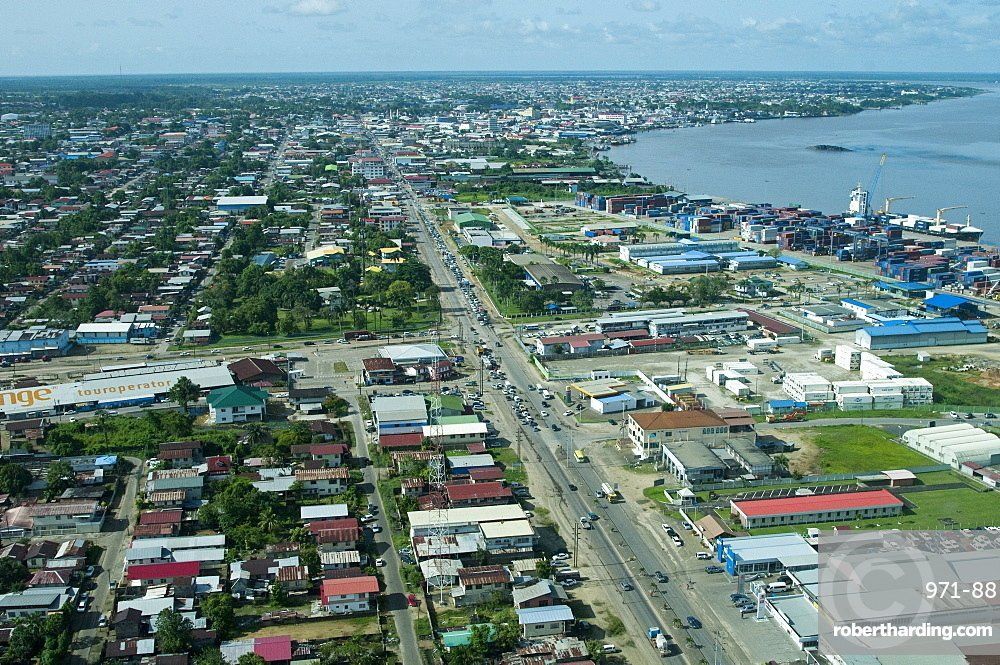 Aerial view of a coastal city with a long road running through it, next to a river. Buildings are densely packed.