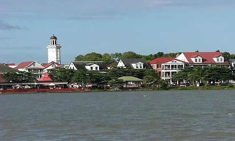 Waterfront view of Paramaribo, Suriname, with colonial-style buildings, including a white clock tower, against a blue sky.