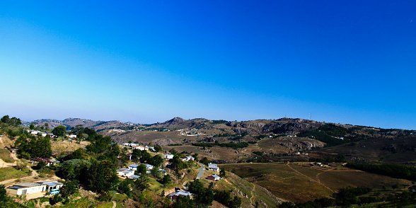 A clear blue sky over a mountainous landscape. Small houses and green trees dot the hillsides.
