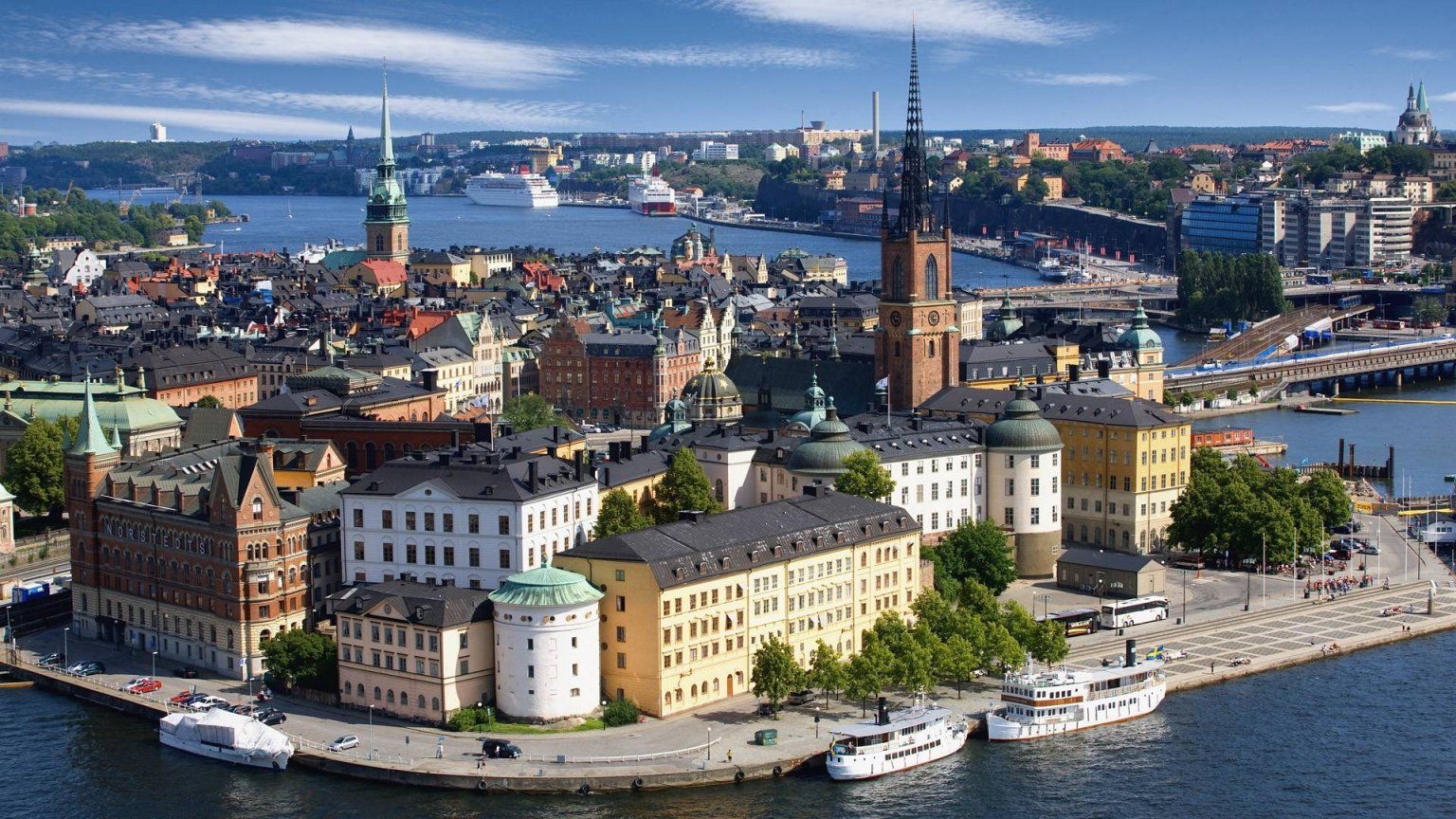 Panoramic view of Stockholm, Sweden, with historic buildings, waterways, and boats under a blue sky.