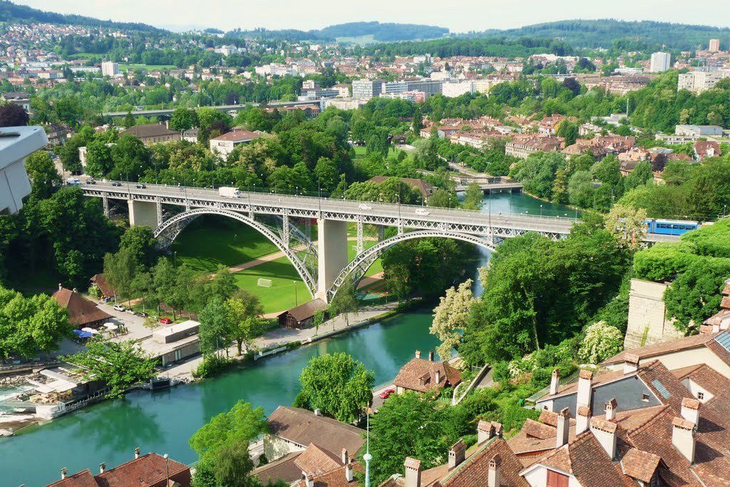 A scenic view of Bern, Switzerland, with a river flowing under a bridge and through the city.