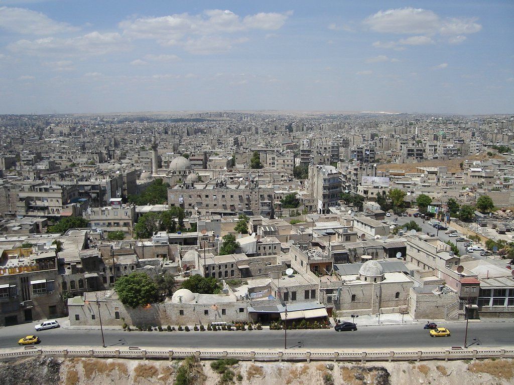Overhead view of a densely populated city in Amman, Jordan, with mostly beige buildings and a road in the foreground.