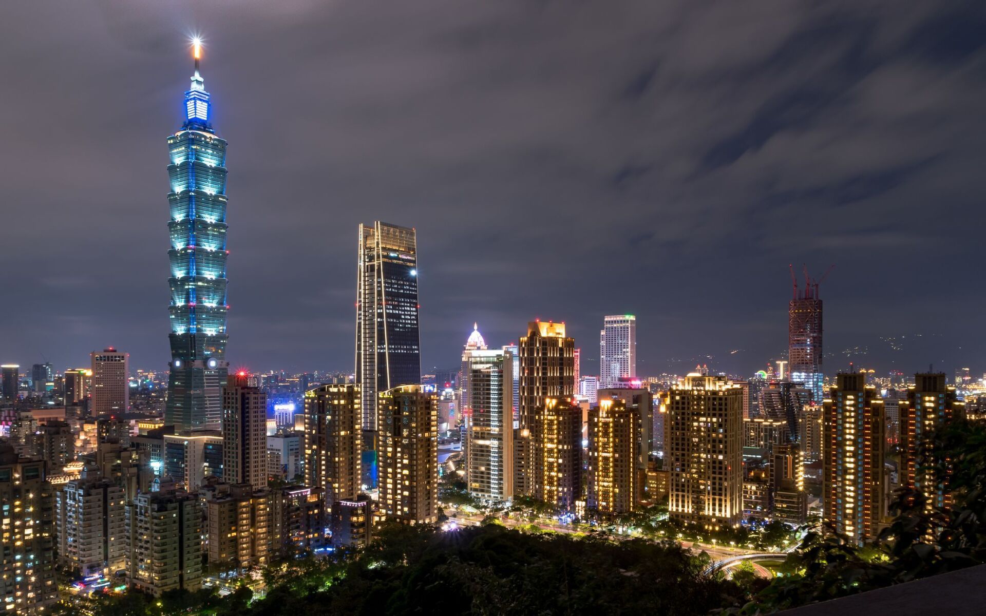 Nighttime view of Taipei, Taiwan, skyline featuring the illuminated Taipei 101 skyscraper and other buildings, with city lights against a dark sky.