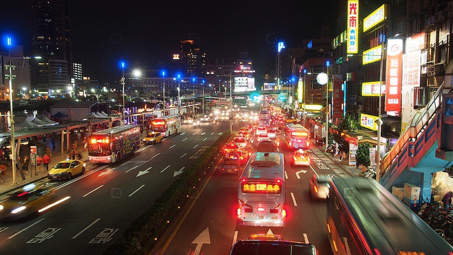 Nighttime view of a busy city street in Taiwan, with cars, buses, and storefronts illuminated by bright lights.