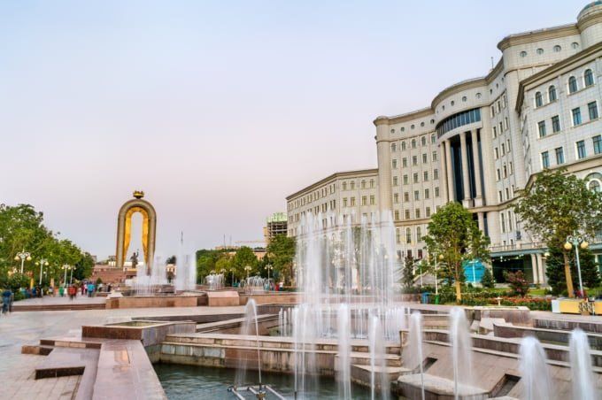 Fountains in front of a large, ornate building in Tashkent, Uzbekistan, with a golden arch monument in the background.