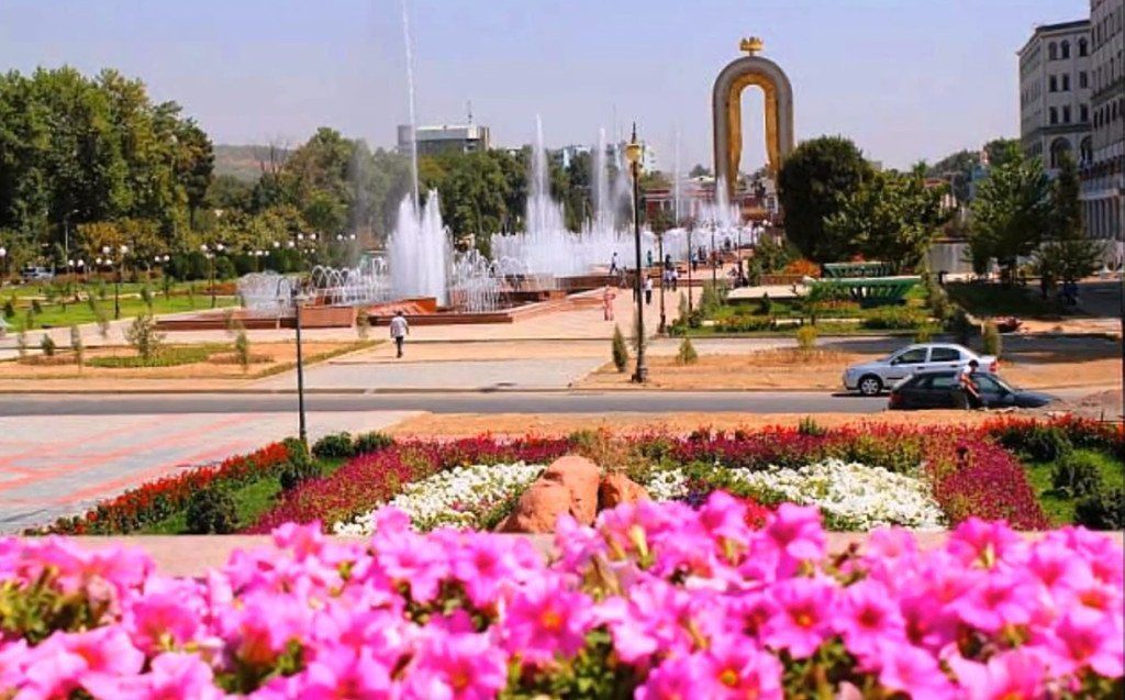 Pink flowers in foreground; fountains, park, and arch in background; Tashkent, Uzbekistan.