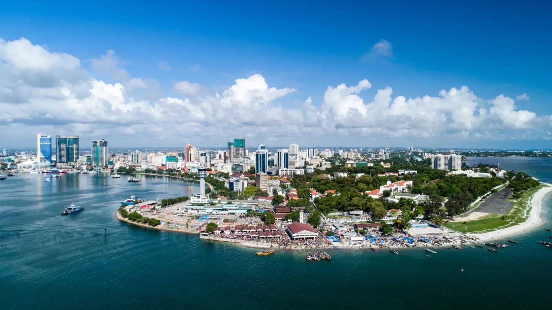 Aerial view of Dar es Salaam, Tanzania. A coastal city with skyscrapers and a central island, under a bright blue sky.