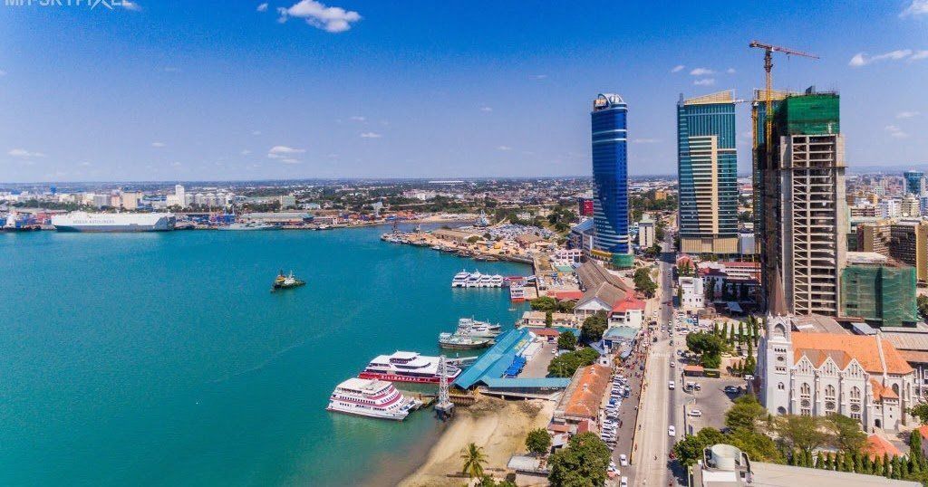 Aerial view of Dar es Salaam waterfront, Tanzania, with a turquoise ocean, boats, modern skyscrapers, and a port.
