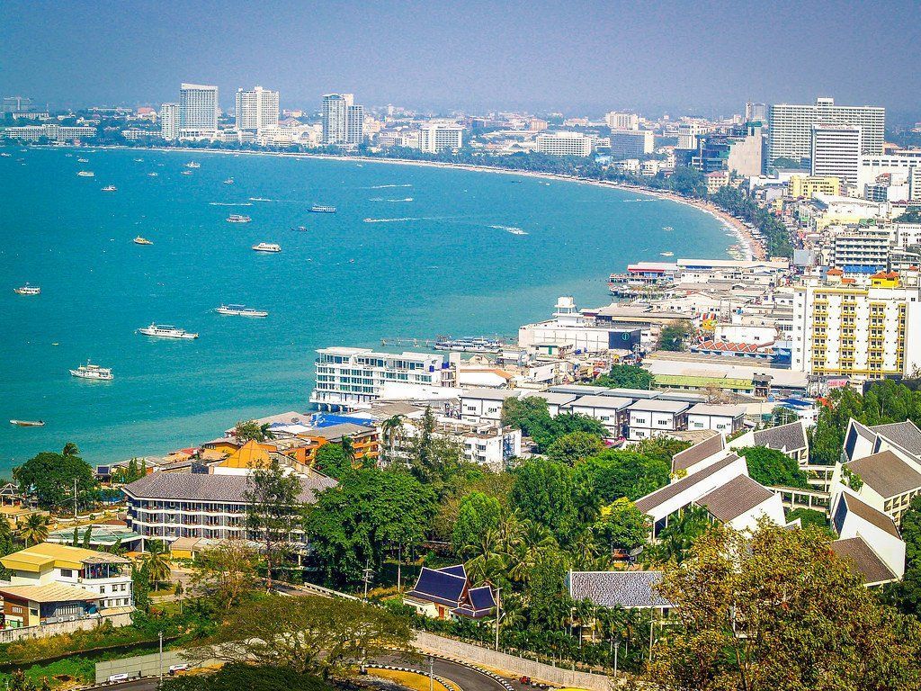 Pattaya, Thailand coastal cityscape with a blue ocean, beach, buildings, and boats under a sunny sky.